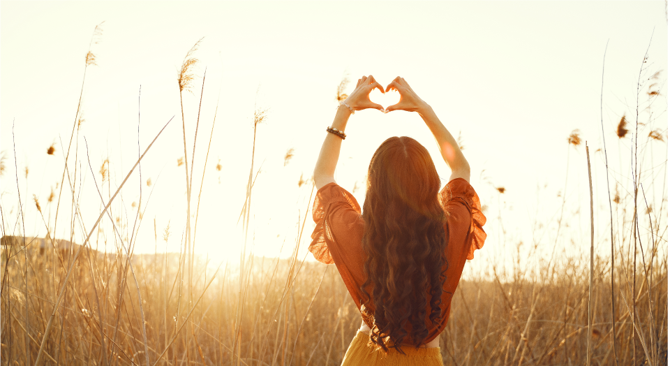 Mujer haciendo con las manos una forma de corazón en un campo durante un atarcer